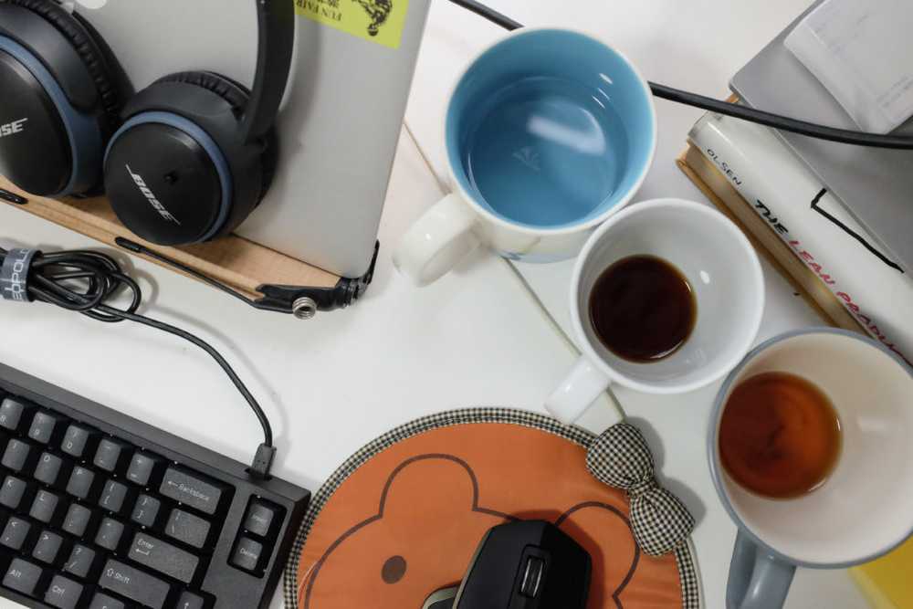 desktop filled with laptop and coffee mugs from working from home